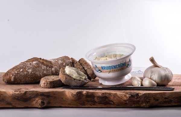 Bedrukt bakje kruidencrème naast brood en knoflook op een houten plank